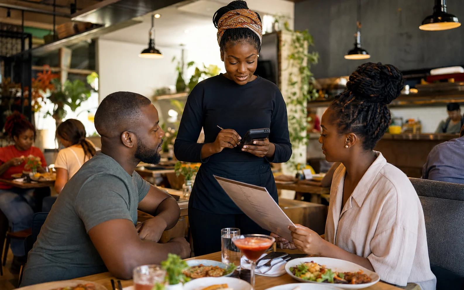 Restaurant server entering an order on a handheld device beside seated diners